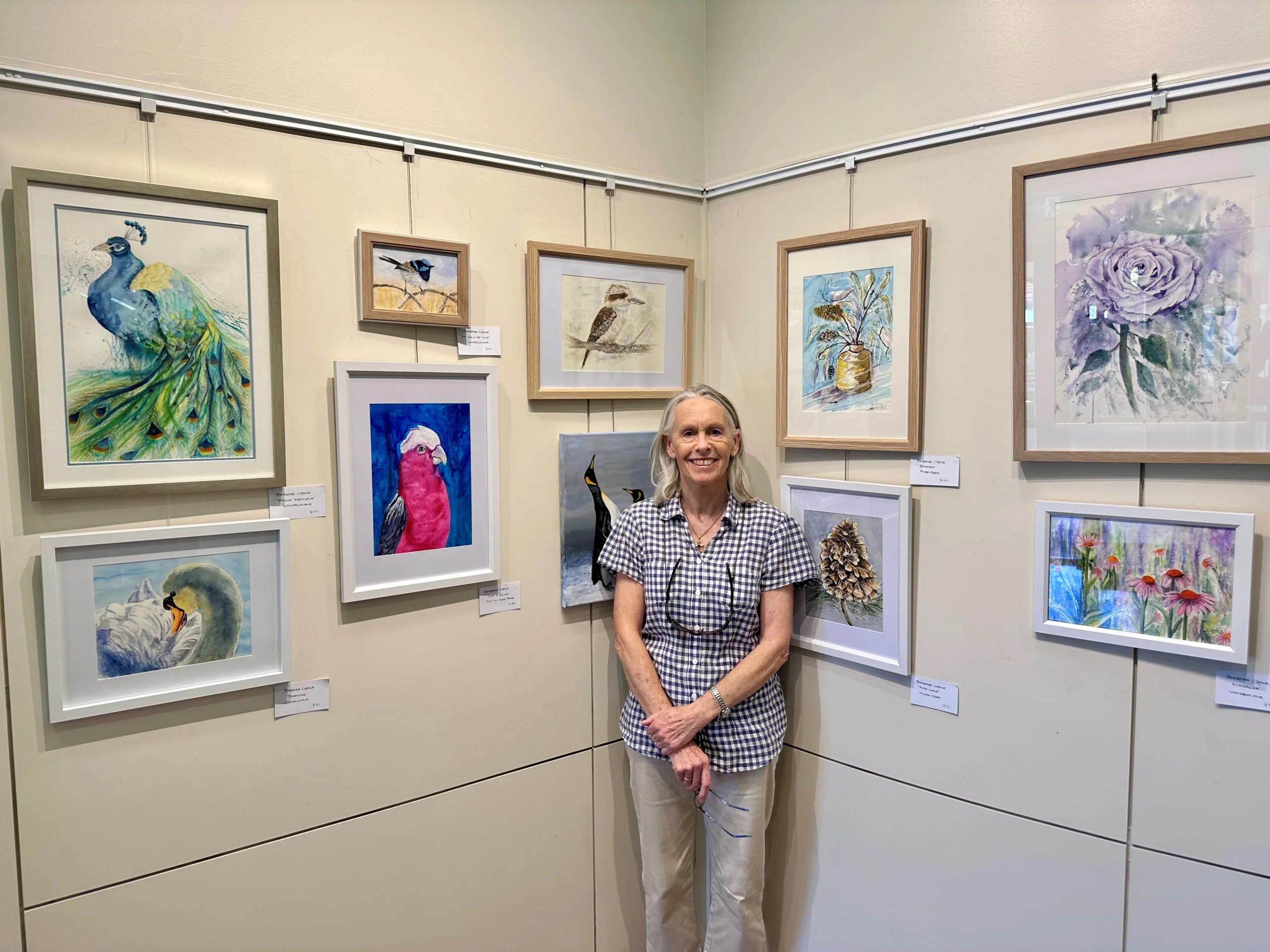 Artist Barbara Crane poses in front of an exhibition of her artworks, which feature birds and flowers.