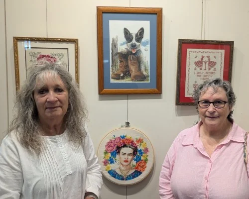 Two crafters pose in front of their cross-stitch work at Tumut Library