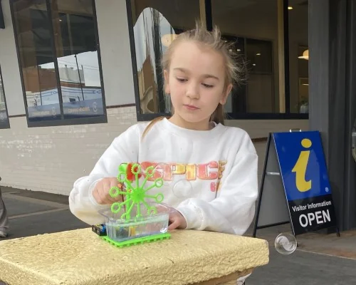 A girl plays with a bubble machine she has made.