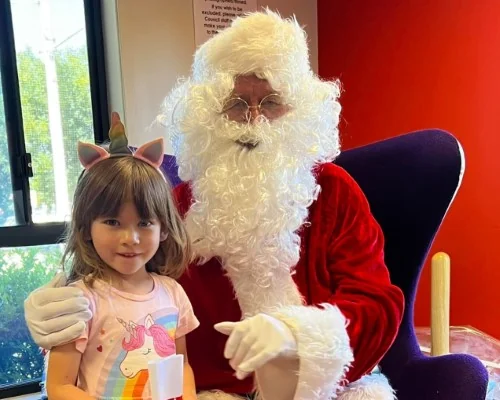 Image of child wearing unicorn horns posing with Santa at a Christmas storytime at the library