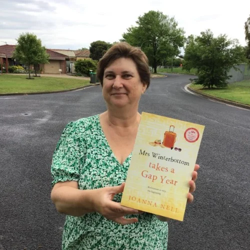 A library staff member poses with Mrs Winterbottom Takes a Gap Year by Joanna Nell