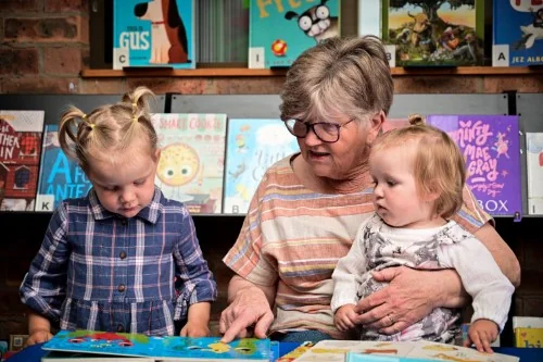 A grandparent reads to two young grandchildren in the library.