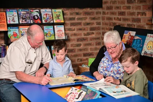 Grandparents reading to their grandchildren in the library.