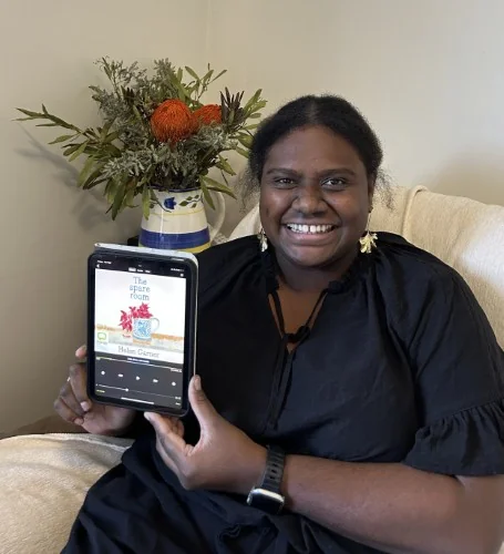 A library staff member holds up the audiobook of The Spare Room by Helen Garner on a device.