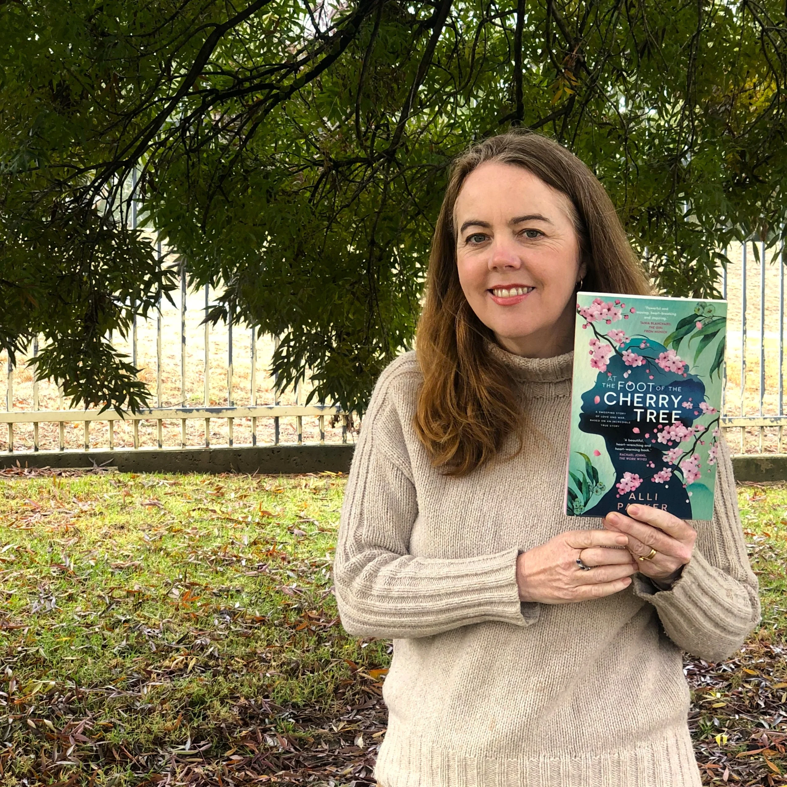 A library staff member holds up At the Foot of the Cherry Tree by Alli Parker