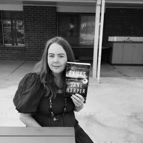 A black and white photo of ibrary staff displaying the book Exiles, by Jane Harper