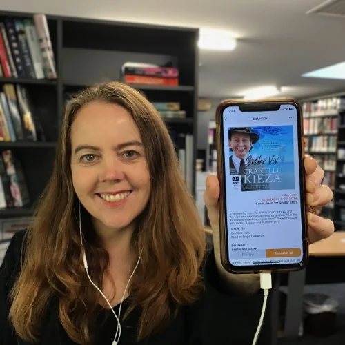 A library staff member displays the audiobook of Sister Viv by Grantlee Kieza on a phone.