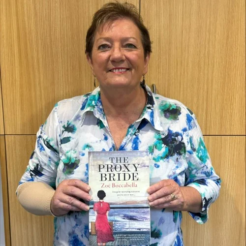 A library staff member holds up a copy of The Proxy Bride by Zoe Boccabella