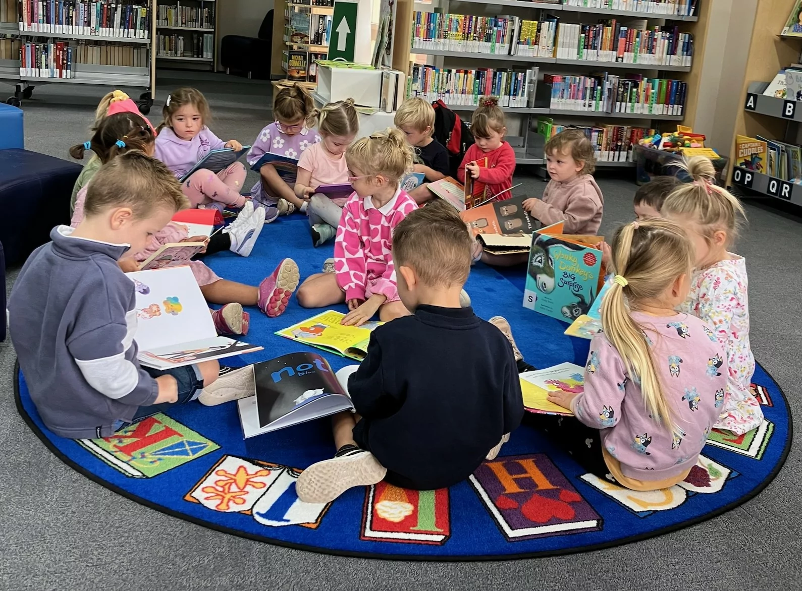 Preschoolers sitting on a mat looking at picture books in Mulwala Library