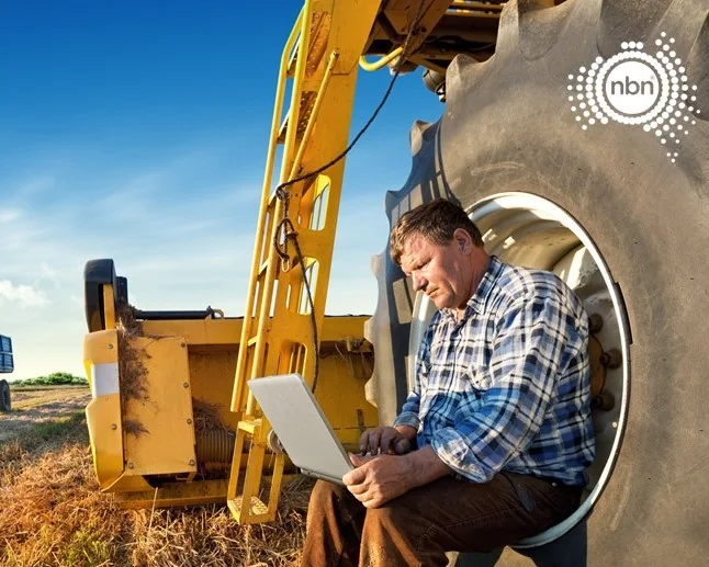 Farmer using a laptop out in a paddock, resting on a tractor tyre