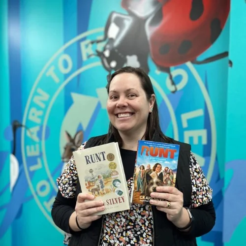 A library staff member poses with the book and movie cover of Runt by Craig Silvey