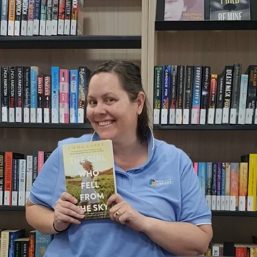 A library staff member poses with The Girl Who Fell From the Sky by Emma Carey.