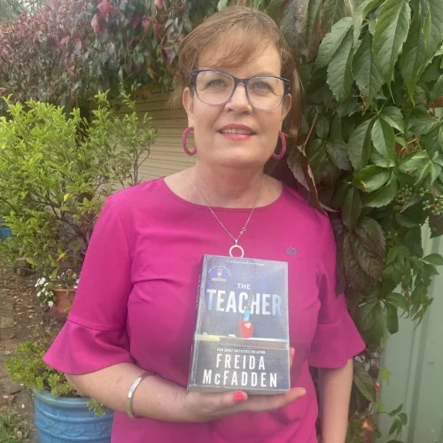 A library staff member stands outside holding The Teacher by Frieda McFadden