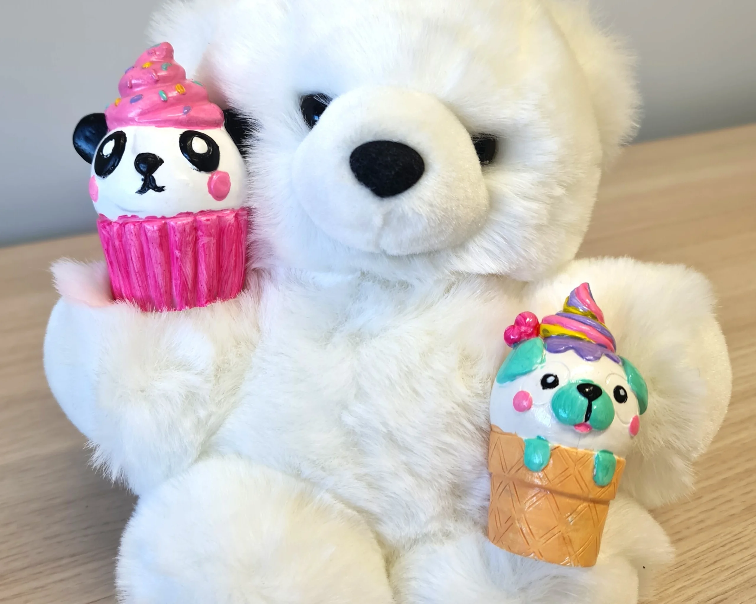 A teddy bear holds a painted plaster cupcake and icecream
