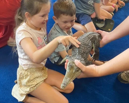 Two kids pat a crocodile at a reptile show.