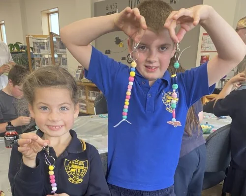 Two kids hold up bag tags they have made from beads.