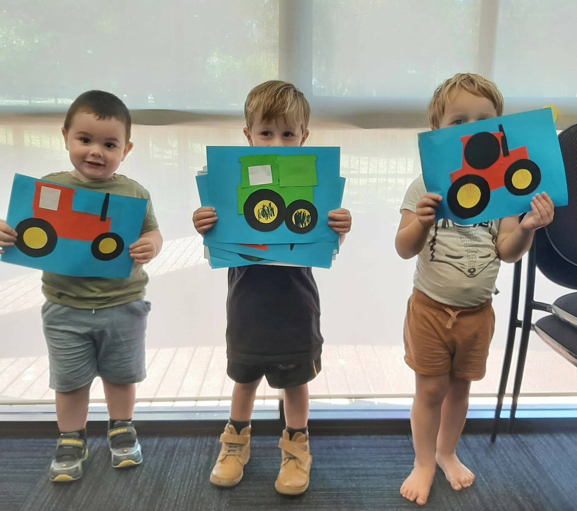 Three preschool aged boys holding up their tractor craft.