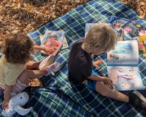 Children read books on a picnic rug in the park!