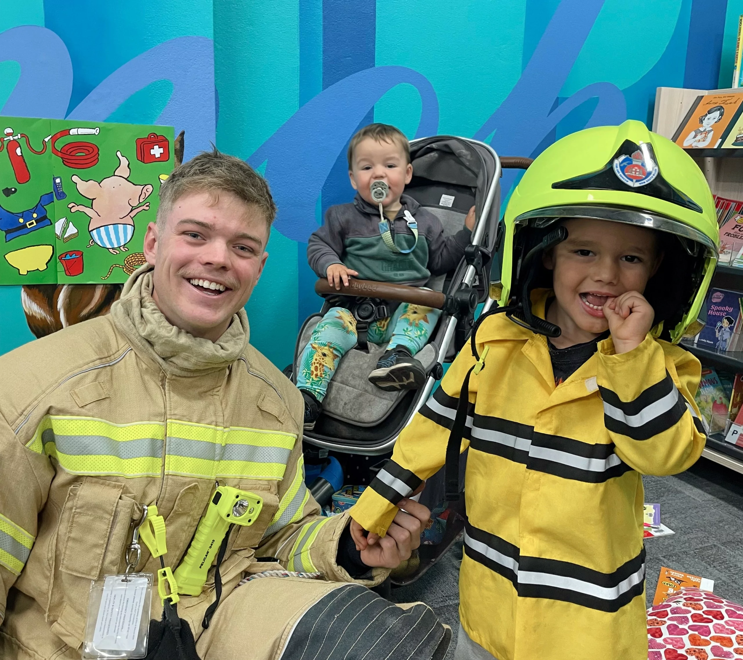 Child wears fire helmet and poses with fireman wearing fire helmet.