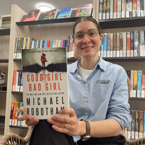 A library staff member displays the book, Good Girl, Bad Girl by Michael Robotham.