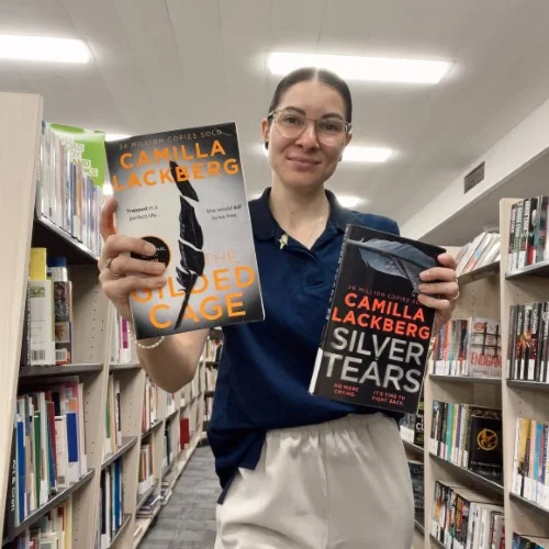 A librarian holds up The Gilden Cage and Silver Tears by Camilla Lackberg