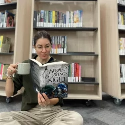 Wendy Manning from Temora library sits on the floor with a cuppa reading The Serpent & the Wings of Night