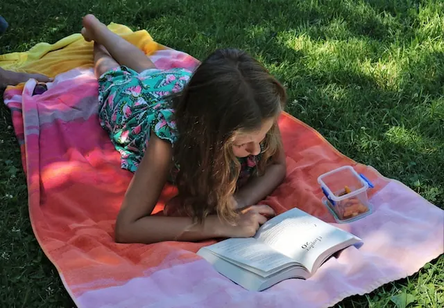 A girl lies on a towel on the grass reading