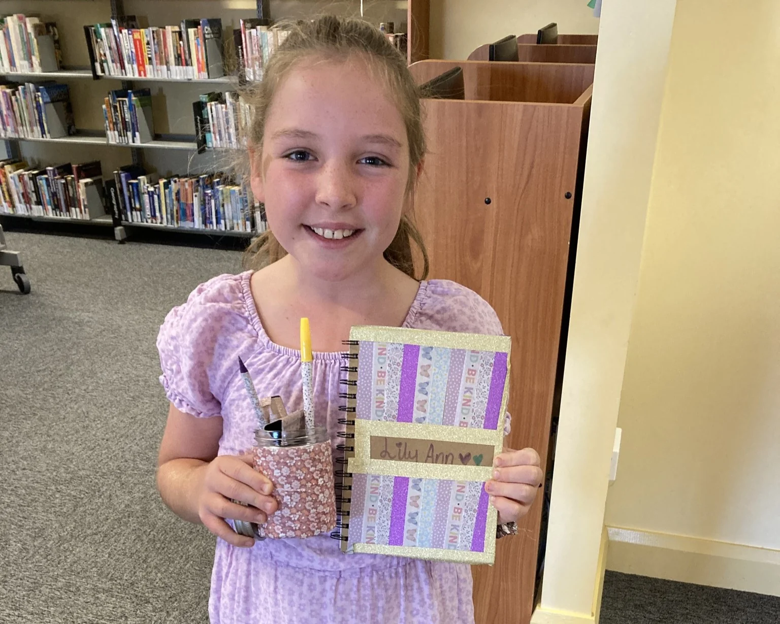 A girl holds up a notebook and jar pencil holder she has decorated with washi tape.